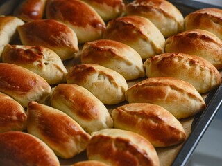 A close-up shot of golden-brown freshly baked russian pirozhki arranged on a baking sheet.