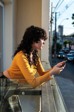 Young woman reading smartphone notifications in balcony