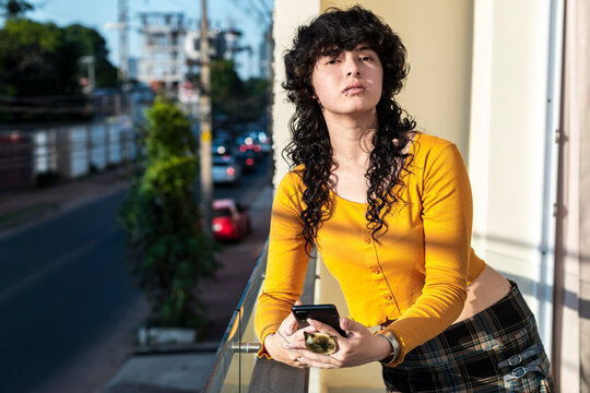 Latina teenager with direct gaze and easy posture holding smartphone 