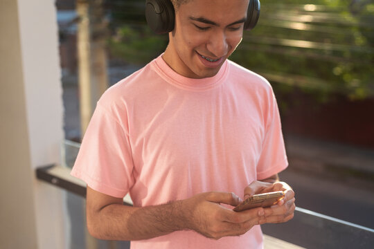 Young man focused in music and social media on sunlit urban balcony - Powered by Adobe