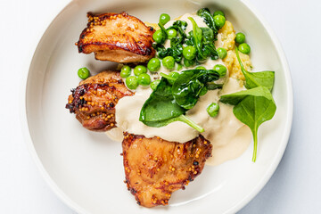 Grilled chicken with creamy sauce, fresh greens, and vibrant peas makes a delightful dish