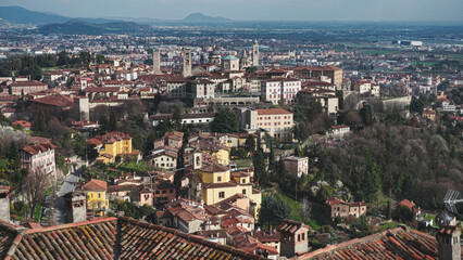 An Italian village rests on a hillside, its red-tiled roofs contrasting beautifully with the surrounding green slopes and scenic mountain backdrop.