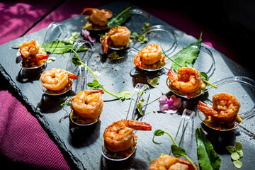 Shrimp appetizers are beautifully arranged on a slate platter, garnished with herbs and flowers