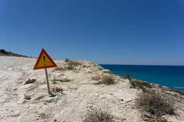 Fototapeta premium Segnale stradale di pericolo, forma triangolare, giallo e rosso con punto esclamativo, sulla scogliera bianca di Kalamaki , isola di Creta