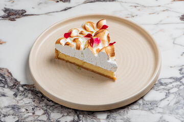 A beautiful piece of lemon meringue pie sits on a smooth plate, garnished with colorful flowers