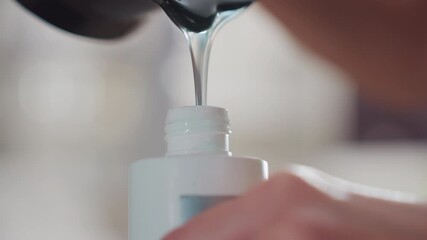 close-up pouring clear developer into bottle, caucasian stylist steady hands measuring slow drip with soft studio lighting, professional salon counter, label visible, precision technique
