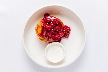 A fluffy pancake sits invitingly on a plate, topped with vibrant cherries and a side of cream