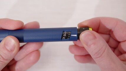 Woman's hands holding insulin syringe pen, twisting plunger to dial dose for diabetes treatment close-up - Powered by Adobe