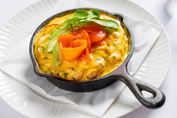 A cast iron skillet holds a creamy dish topped with fresh herbs and colorful veggies