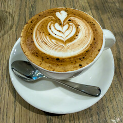 A delightful cappuccino with elegant multiple heart latte art, served in a white cup on a rustic wooden table.