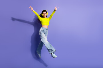 Young woman dancing in neon top with headphones jumping against purple background for fashion lifestyle advertising