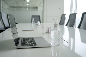 Hybrid workplace with modern office table featuring laptop hand sanitizer and conference chairs in bright meeting room promoting clean and productive environment