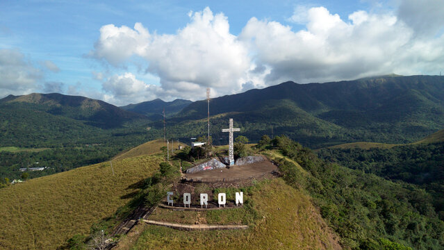 December 2 2025 in Palawan Philippines. Aerial view of Mt Tapyas summit featuring white Coron sign and metal cross overlooking green mountains under blue cloudy sky.