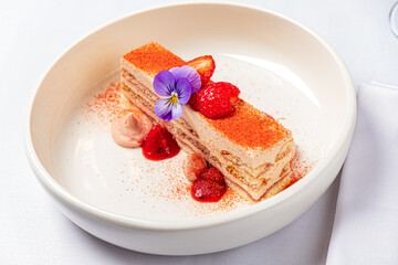 Layers of cream and cake topped with strawberries and a flower create a stunning dessert display