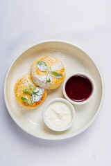 Sweet pastries dusted with sugar alongside creamy topping and vibrant berry sauce