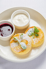 Fluffy pancakes with powdered sugar, mint, cream, and berry sauce