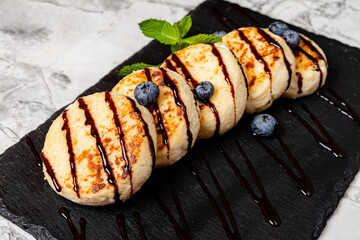 Fluffy pancakes arranged on a slate platter, garnished with blueberries and chocolate drizzle