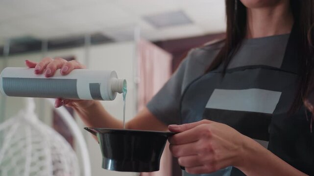 caucasian colorist carefully pouring developer into mixing bowl, closeup hands and bottle, precise measurement in bright salon, focused technique and product texture visible, professional station
