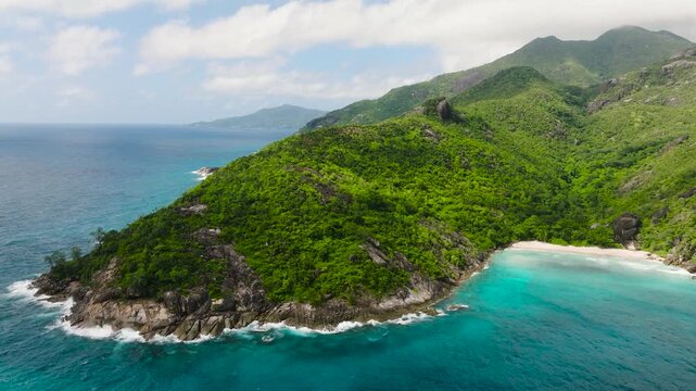 Aerial view of beach nestled between forested mountains and clear sea. Seychelles, Mahe. Anse Du Riz beach. Baie Ternay Marine National Park.