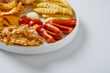 Mix platter consisting of union ring, french fries, sausage, enoky mushrooms, tortilla and served on a plate with mayonnaise and tomato sauce. Copy space snack concept