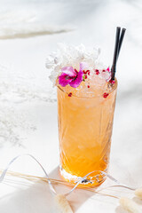 A vibrant cocktail with ice and flowers sits on a sunlit surface, inviting relaxation and enjoyment