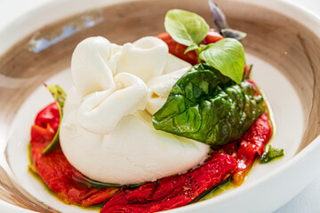 A delicious serving of burrata cheese sits atop roasted red peppers, enhanced with fresh basil