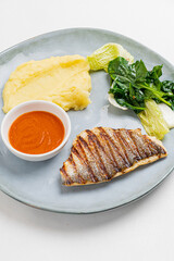 Grilled fish rests alongside creamy mashed potatoes and vibrant greens, highlighting a fresh meal