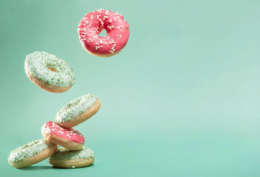 A dynamic stack of six glazed donuts, featuring white with green sprinkles and pink icing, tumbling on the left side of a mint green background with ample empty space on the right