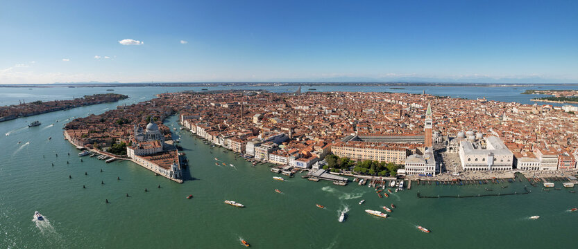 Aerial view of boats glide on the shimmering green waters around Venice's iconic landmarks like St. Mark's Square and Doge's Palace, Venice, Italy.