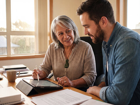 Senior woman and young man collaborating on digital tablet in bright office with natural light