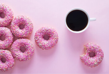 Pink sprinkled donuts arranged in an arrow shape pointing towards a cup of black coffee on a matching pink background