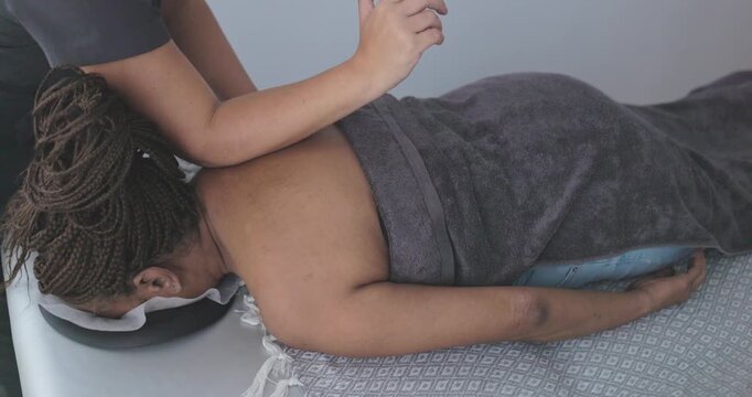 Female chiropractor therapist doing back massage to african senior woman patient inside her studio - Healthcare, wellness and healthy lifestyle concept