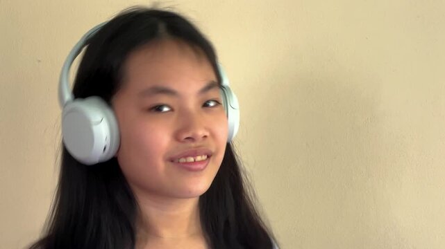 A young girl with headphones, smiling subtly, stands against a plain wall. Ideal for educational or tech-themed content.