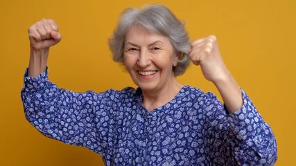 Joyful elderly woman celebrating with raised fist in floral blouse, confident senior woman smiling and flexing arm showing victory and strength