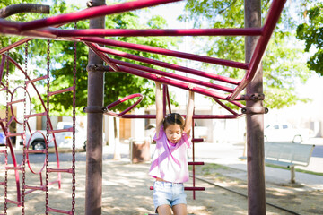 Young girl playing on monkey bars at outdoor playground, enjoying active childhood fun in summer park