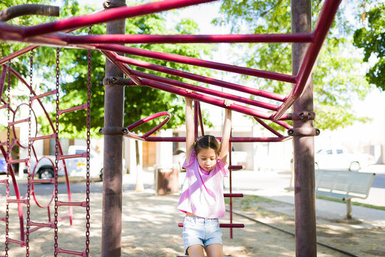 Young girl playing on monkey bars at outdoor playground, enjoying active childhood fun in summer park