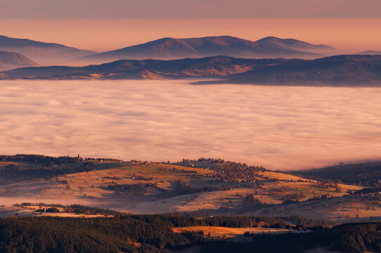 Aerial view of fog-shrouded valleys meet rolling hills and distant peaks under a soft sky, Bystra, Zilina Region, Slovakia.