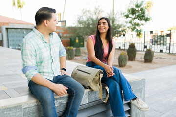 Young man and woman sitting outdoors on a university campus, engaging in a friendly and happy conversation