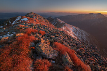Aerial view of rugged mountain peaks kissed by the warm hues of the setting sun, with patches of snow and fiery vegetation, Pribylina, Zilina Region, Slovakia.