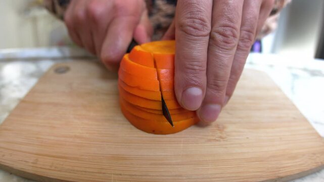 A man cutting persimmons. Slicing persimmons for a salad on a wooden board. Delicious persimmon salad. Healthy eating.