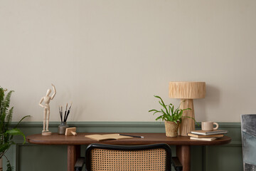 Warm and cozy composition of  workspace interior with wooden desk, rattan armchair, plant in...