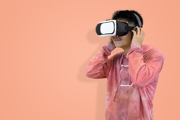 Excited young Asian man wear hoodie reacting with joy while wearing a virtual reality headset, symbolizing the thrilling first experience in studio background