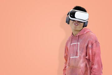 Intense young Asian man in a pink tie-dye hoodie wearing a virtual reality headset and headphones, making a focused or grimacing expression in studio background