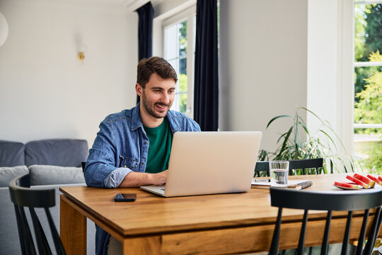 Man working remotely from home on laptop at dinning table
