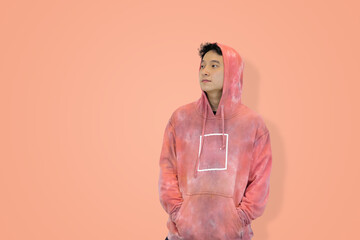 Young Asian man in a pink tie-dye hoodie with the hood up, hands in his pocket, looking contemplative symbolizing casual lifestyle in studio background