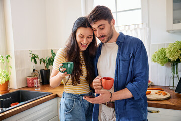 Young couple having morning coffee at home using mobile phone together