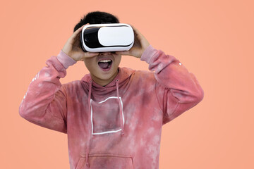 Excited young Asian man wear hoodie reacting with joy while wearing a virtual reality headset, symbolizing the thrilling first experience in studio background