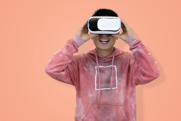 Excited young Asian man wear hoodie reacting with joy while wearing a virtual reality headset, symbolizing the thrilling first experience in studio background
