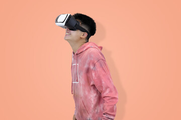 Excited young Asian man wear hoodie reacting with joy while wearing a virtual reality headset, symbolizing the thrilling first experience in studio background