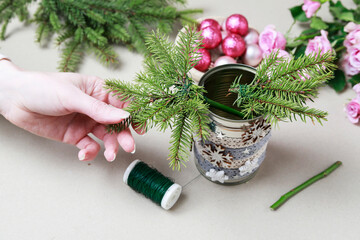 Florist at work: woman shows how to make modern Christmas decoration with fir, roses, pink baubles and decorative stars. The base is classic can. Step by step, complete tutorial.